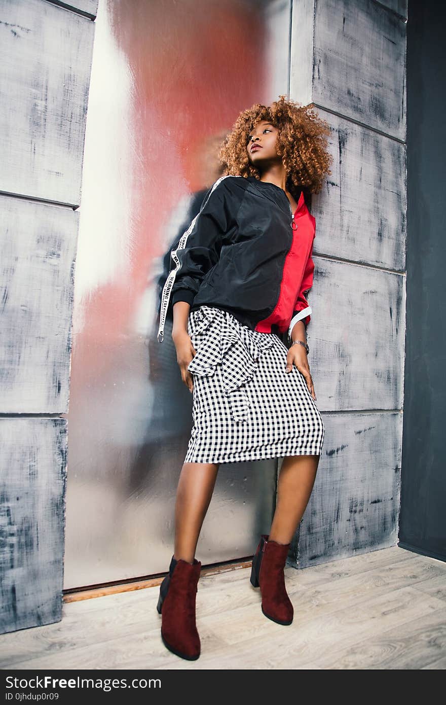 Woman in Black and Red Zip-up Jacket Leaning on Gray Painted Wall