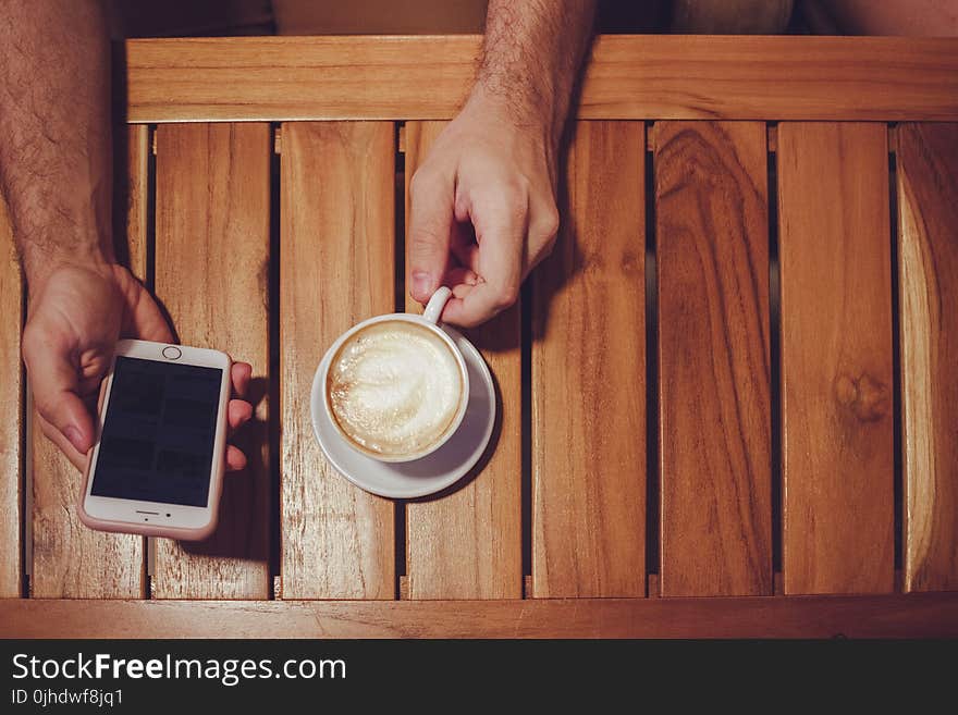 Person Holding Turned Off Gold Iphone 6 With Case and White Ceramic Cup Filled With Latte