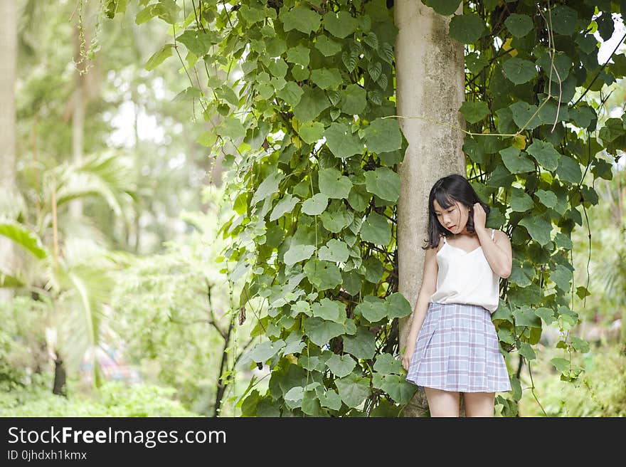 Woman in White Spaghetti Strap Top and Gray Skirt Standing in Front of Tree