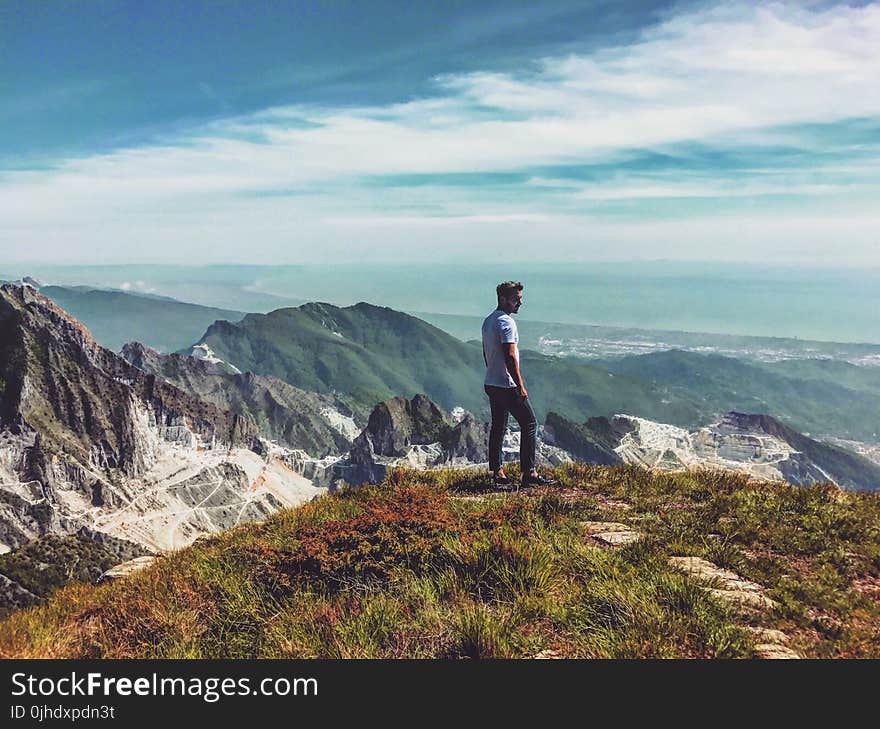 Man Wearing White T-shirt Standing on Mountain Under Blue Cloudy Sky