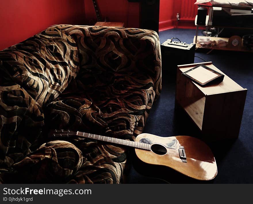 Brown Acoustic Guitar Leaning on Brown Velvet Couch