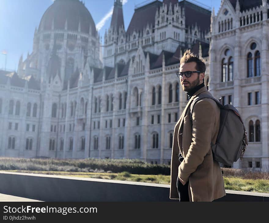 Man Wearing Brown Coat Standing Outside White Mansion