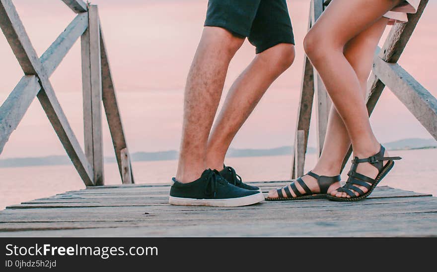 Man in Black Low-top Sneakers Leaning Towards Woman in Black Gladiator Flat Sandals on Dock