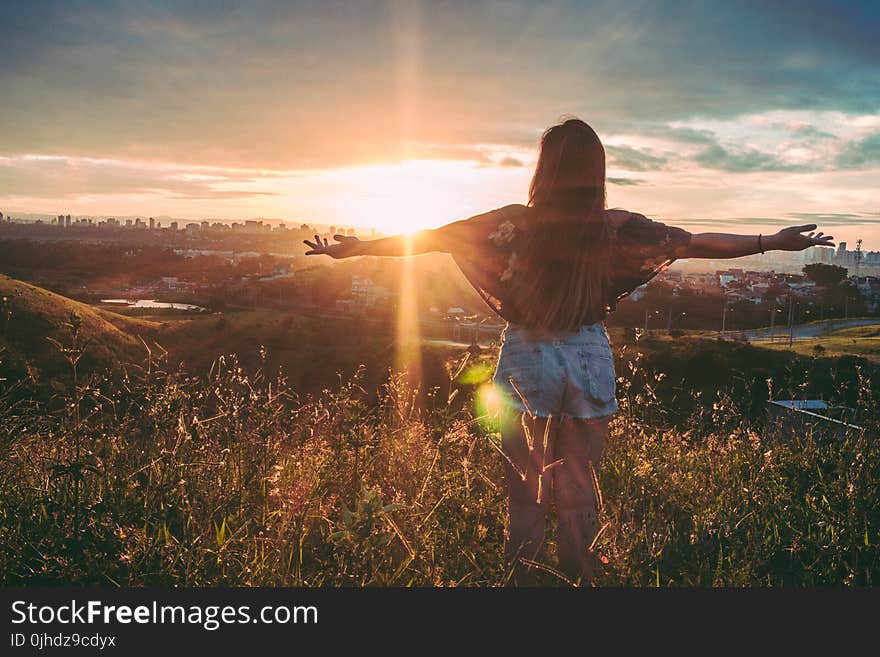 Woman Stands on Mountain over Field Under Cloudy Sky at Sunrise