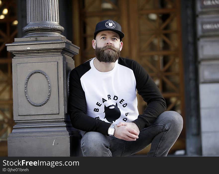 Man in White and Black Pullover Shirt Leaning on Black Post