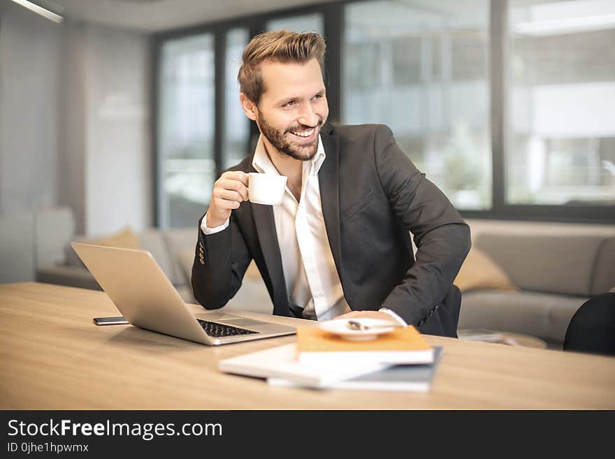 Man Holding White Teacup in Front of Gray Laptop