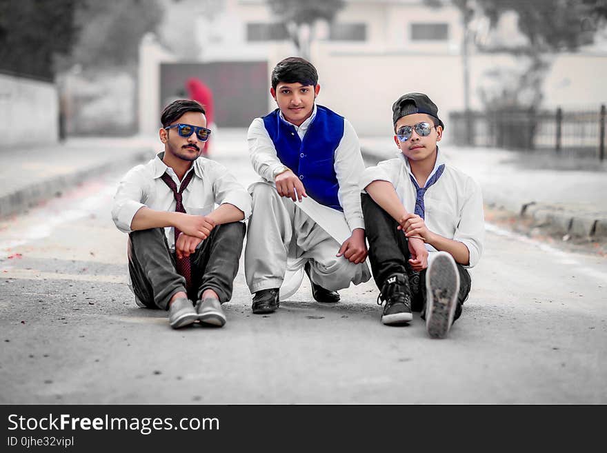 Three Men Sitting on Gray Concrete Road