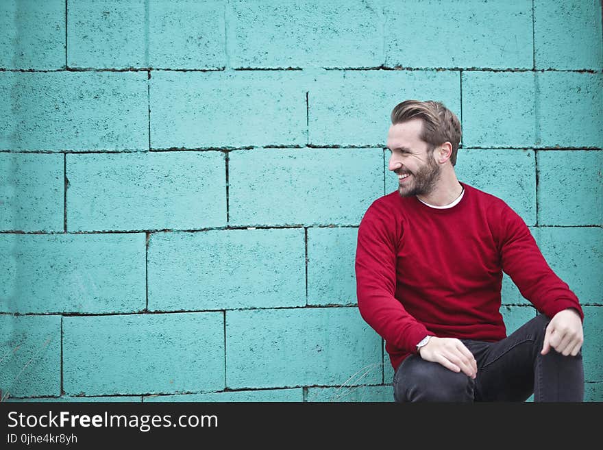 Man Wearing Red Sweatshirt and Black Pants Leaning on the Wall