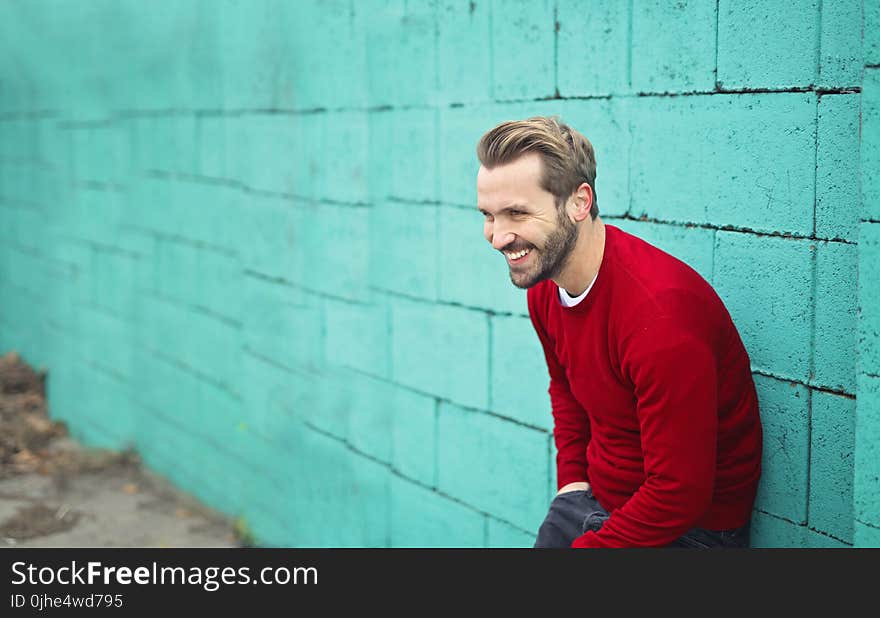 Man Wearing a Red Sweater Leaning on a Blue Wall