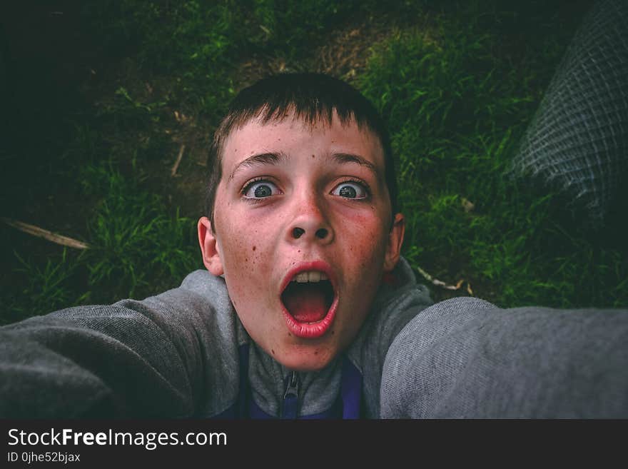 Opened Mouth Black Haired Boy in Gray Full-zip Jacket Standing on Grass Field Taking Selfie