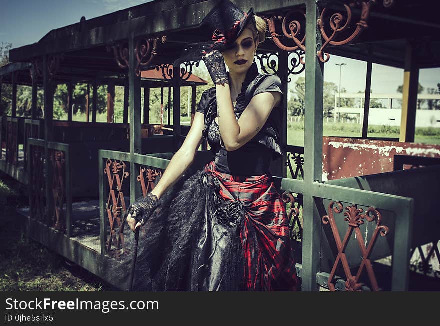 Woman in Black and Red Short-sleeved Dress Standing in Front of Green Steel Structure