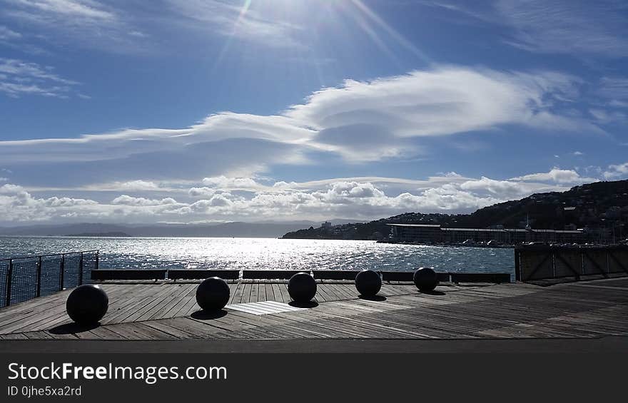 Five Balls Placed on Gray Wooden Platform Near Sea