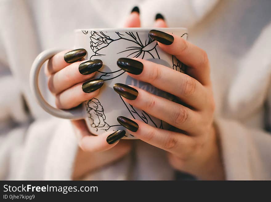 Woman With Black Manicure Holding White and Grey Floral Ceramic Cup