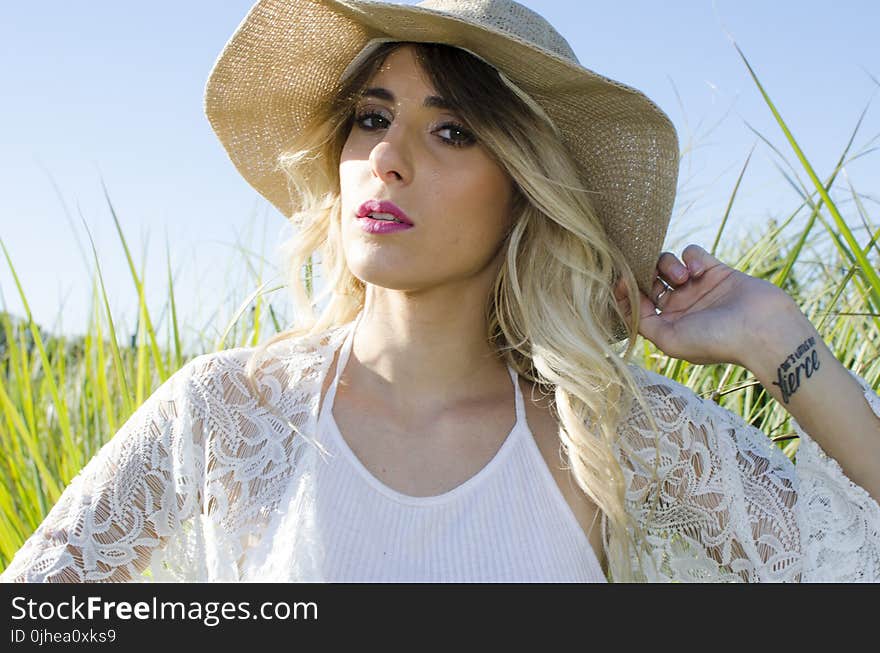 Woman Wearing Brown Hat and White Cardigan Standing in Middle of Grass Field