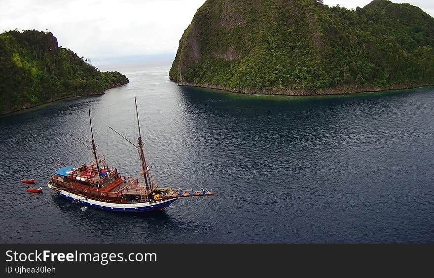 Brown Ship Near Mountain Covered With Green Trees