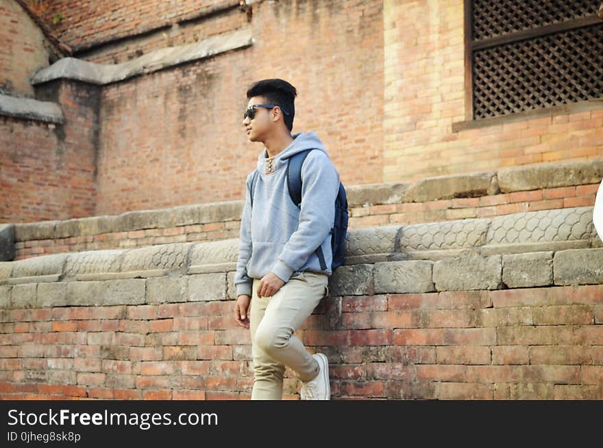 Man in Heather-grey Pullover Hoodie and Beige Pants Standing Near Brick Wall