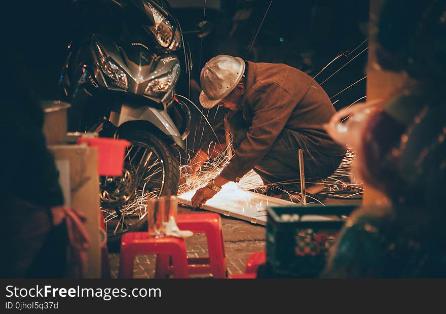 Shallow Focus Photography of Man in Brown Jacket Wearing Gray Hat in Front of Motorcycle