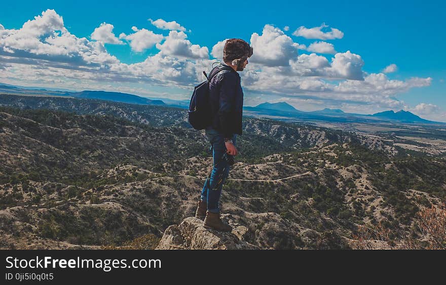 Man Wearing Blue Jeans Standing on Gray Stone Fragment Under Cloudy Sky