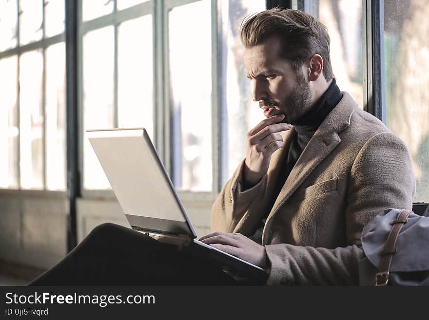 Man Wearing Brown Jacket and Using Grey Laptop