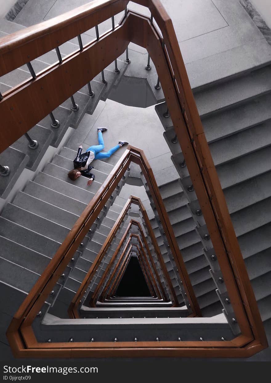 Person In Black Jacket And Blue Denim Pants Laying On Spiral Staircase