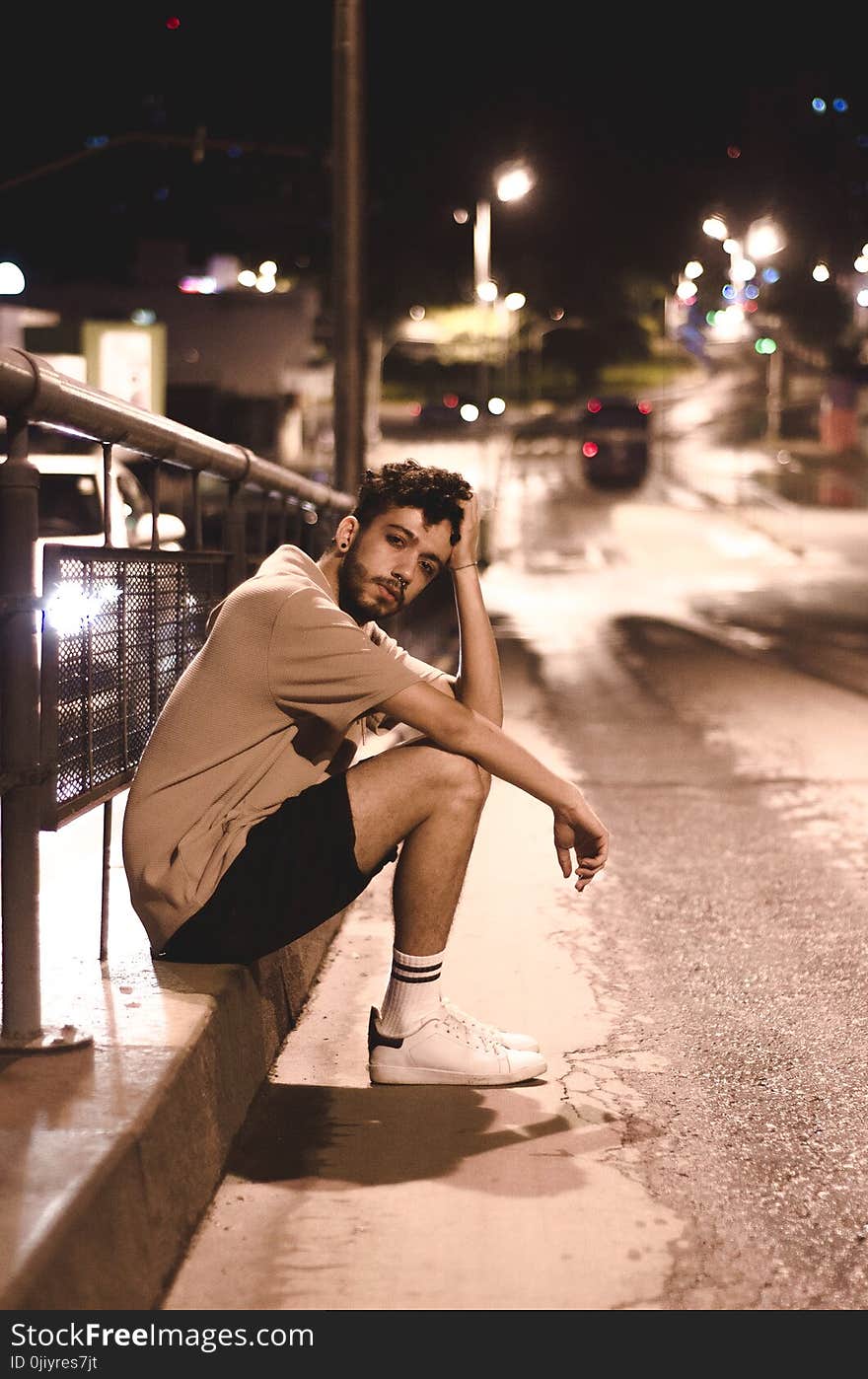 Man Wears Brown Shirt and Black Shorts Seats Beside Black Street Post