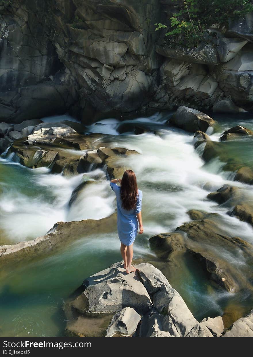 Woman in Blue Long-sleeved Dress Standing in Middle of Rock With Raging Water