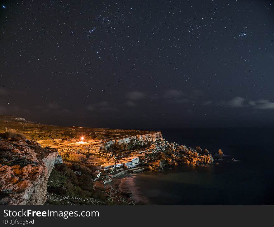 Rock Cliff Near Body of Water Under Clouds and Sky during Nighttime