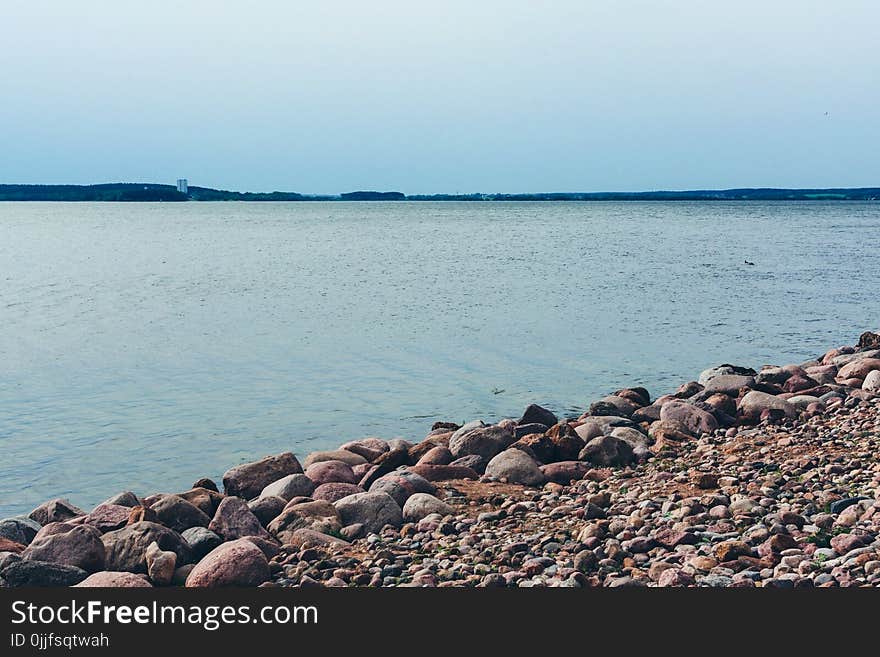 Rock Lot by the Body of Water Under Blue Sky