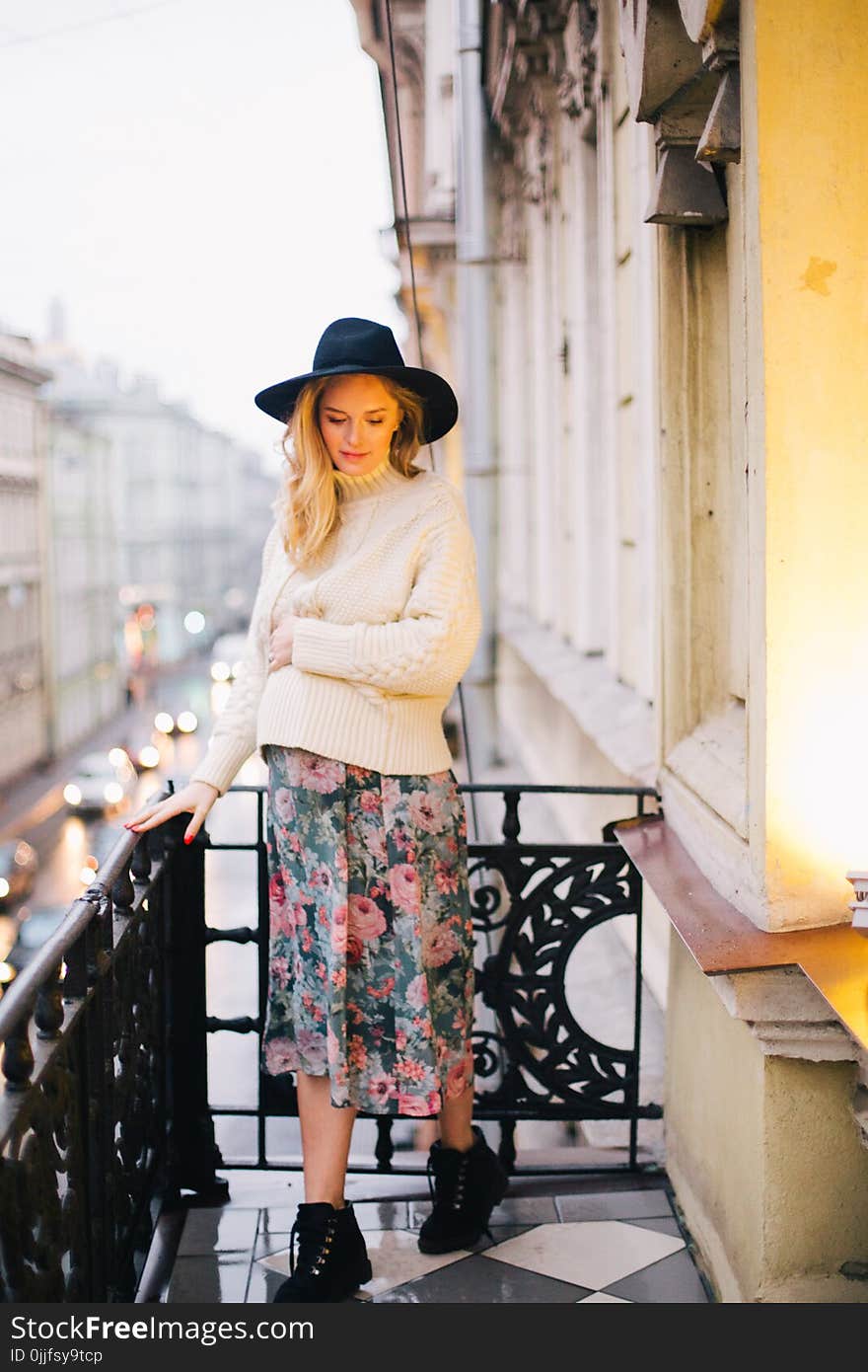 Pregnant Woman Wearing White Sweater and Multicolored Floral Skirt Standing on Balcony