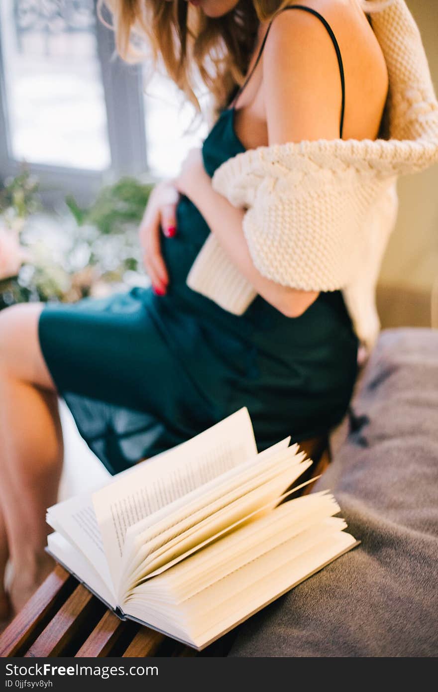 Selective Focus of Pregnant Woman in Black Spaghetti Strap Dress Sitting on Chair Beside Opened Book