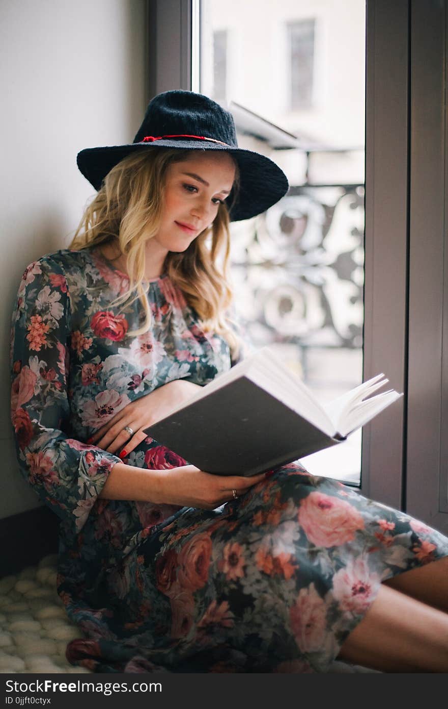 Pregnant Woman Wearing Green, Red, and White Floral Dress Reading a Book Near Window