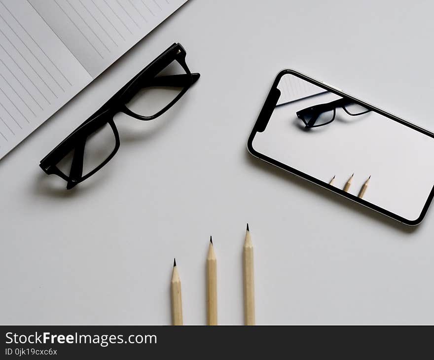 Three Pencils, Eyeglasses, and Smartphone on White Table