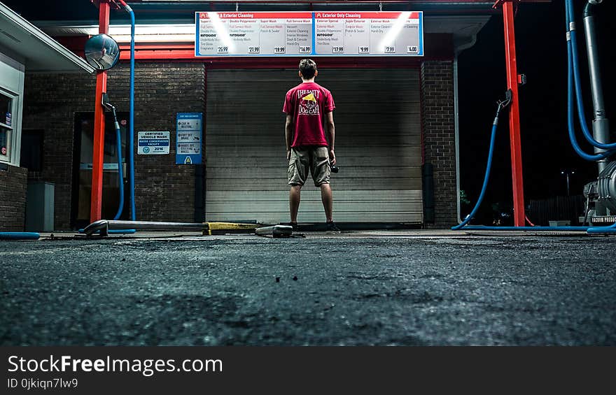 Man in Red Shirt and Brown Shorts Standing Near Wall