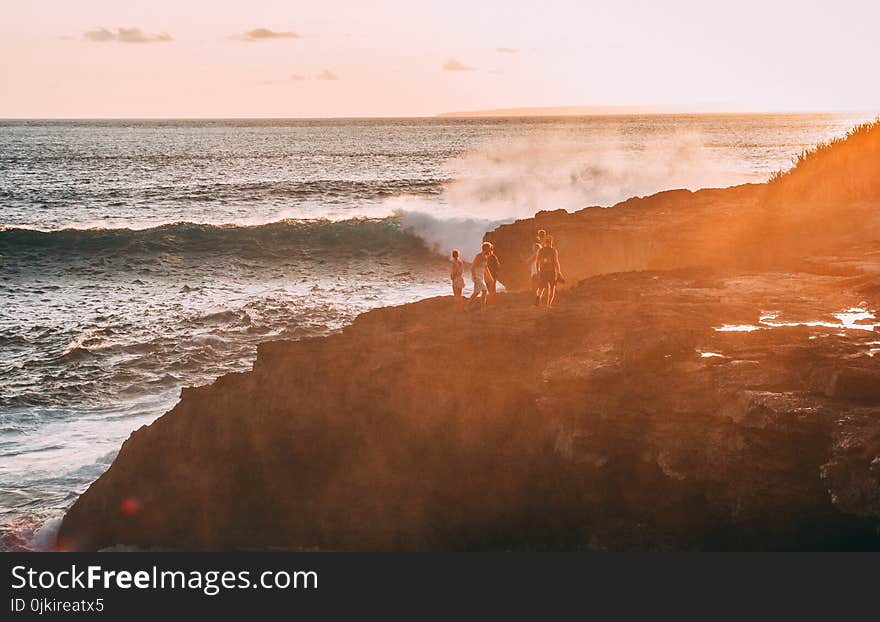 People Standing on Cliff Near Body of Water Golden Hour Photography