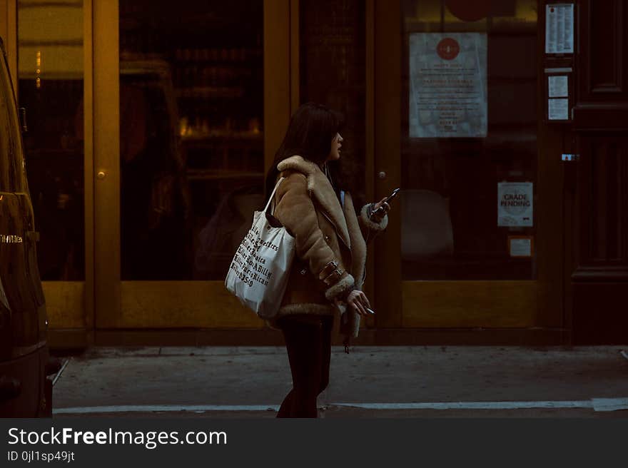 Woman Carrying White Tote Standing Beside Brown Glass Door Building