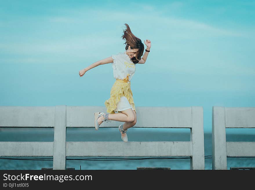 Jumpshot Photography of Woman in White and Yellow Dress Near Body of Water