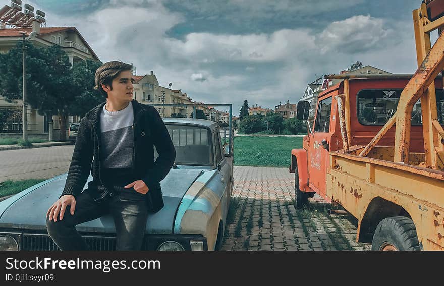 Man In Black Zip-up Jacket On Blue Car Beside Orange Truck