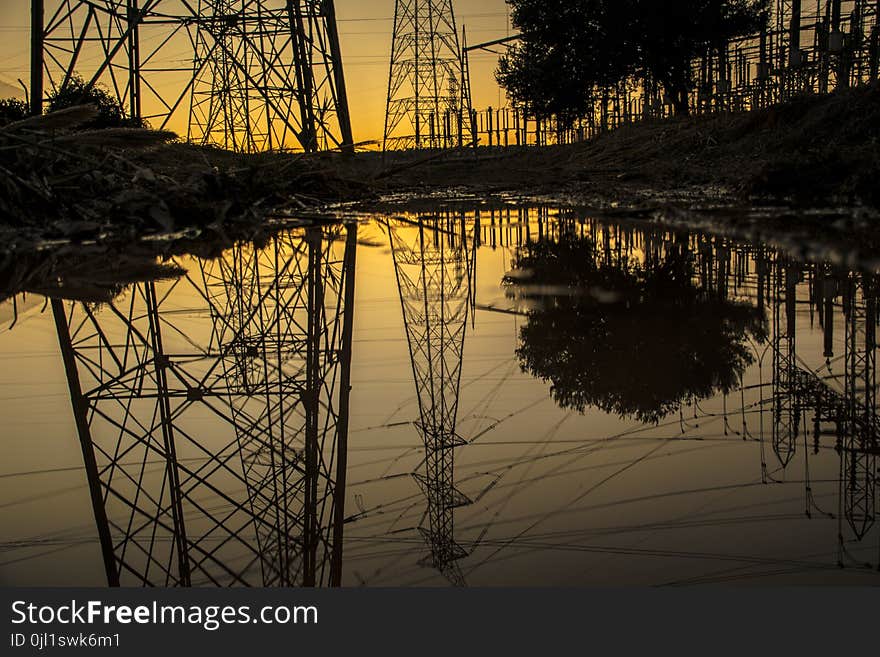 Silhouette of Trees and Electric Tower Reflecting on Body of Water during Sunset