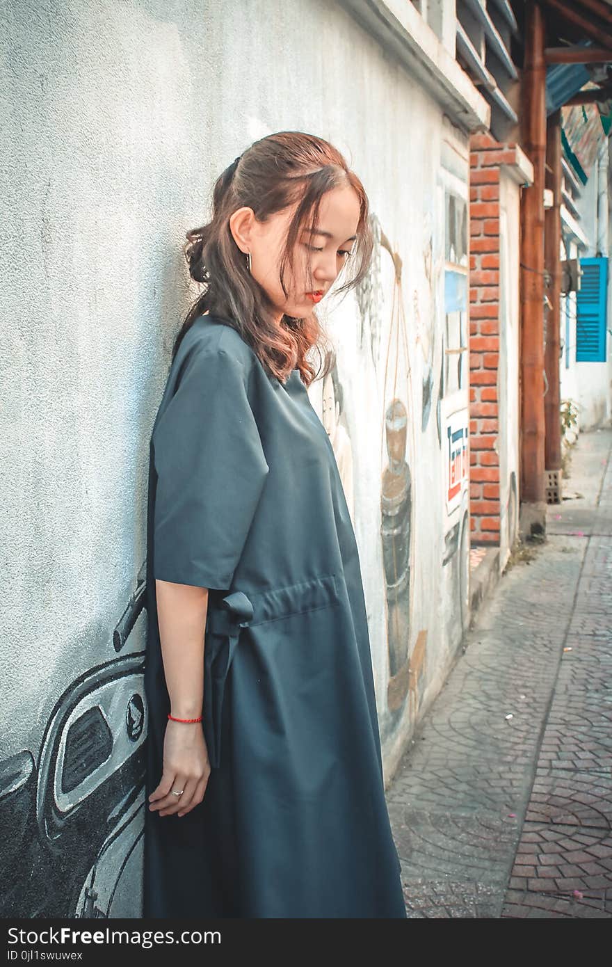 Woman Wearing Gray Coat Leaning on Gray Wall With Graffiti