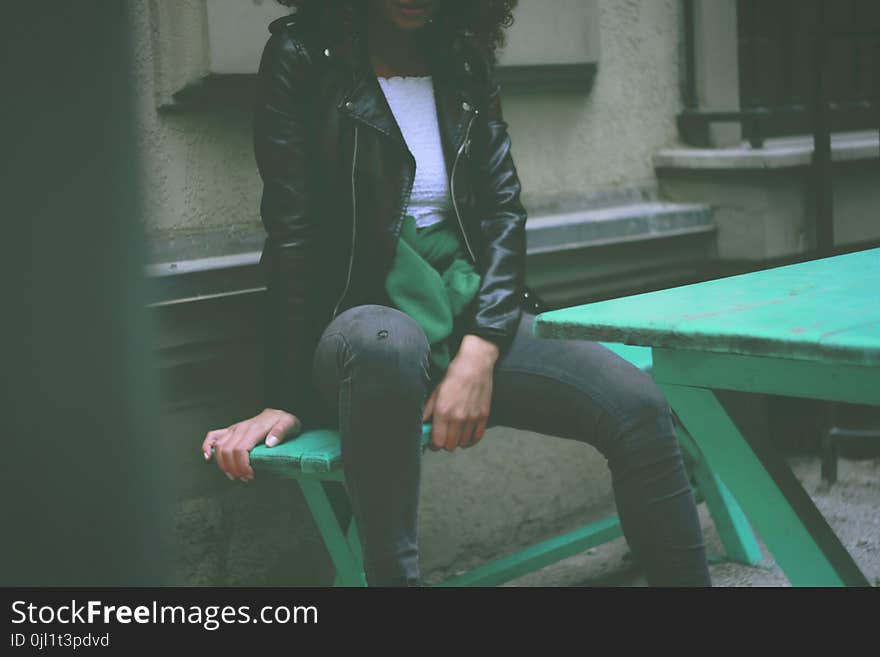 Woman Wearing Black Leather Jacket Sitting on Green Wooden Bench