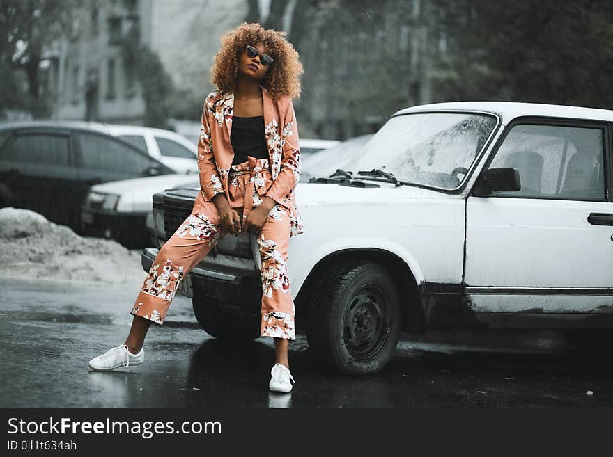 Woman in Pink-and-white Floral Jacket and Pants Sitting on Hood of Car