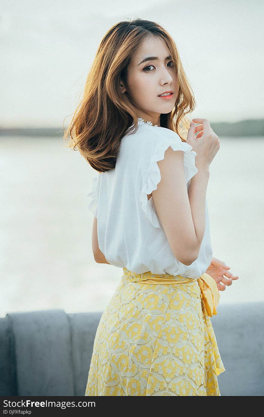 Photo of Woman Wearing White Sleeveless Shirt and Yellow Floral Skirt Near Body of Water