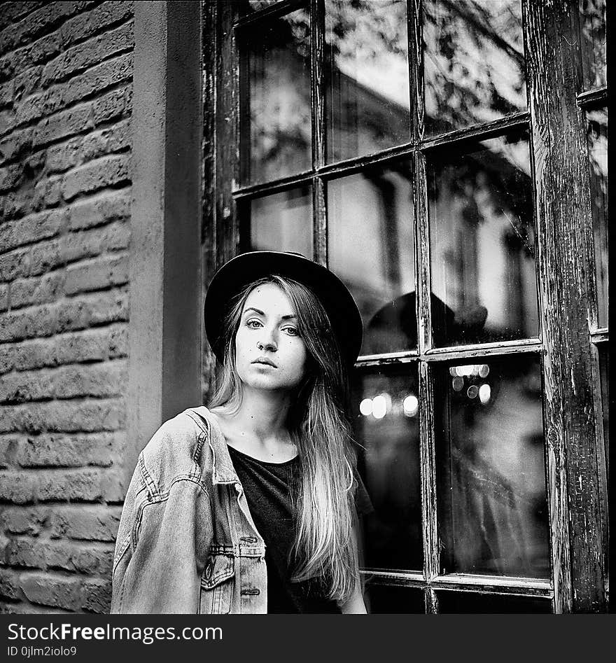 Grayscale Photo of Women&#x27;s Denim Jacket and Hat Leaning on Window