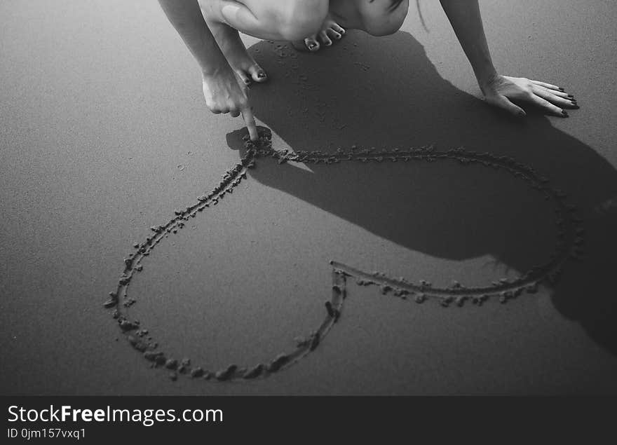 Grayscale Photo of Woman Drawing Heart on Sand