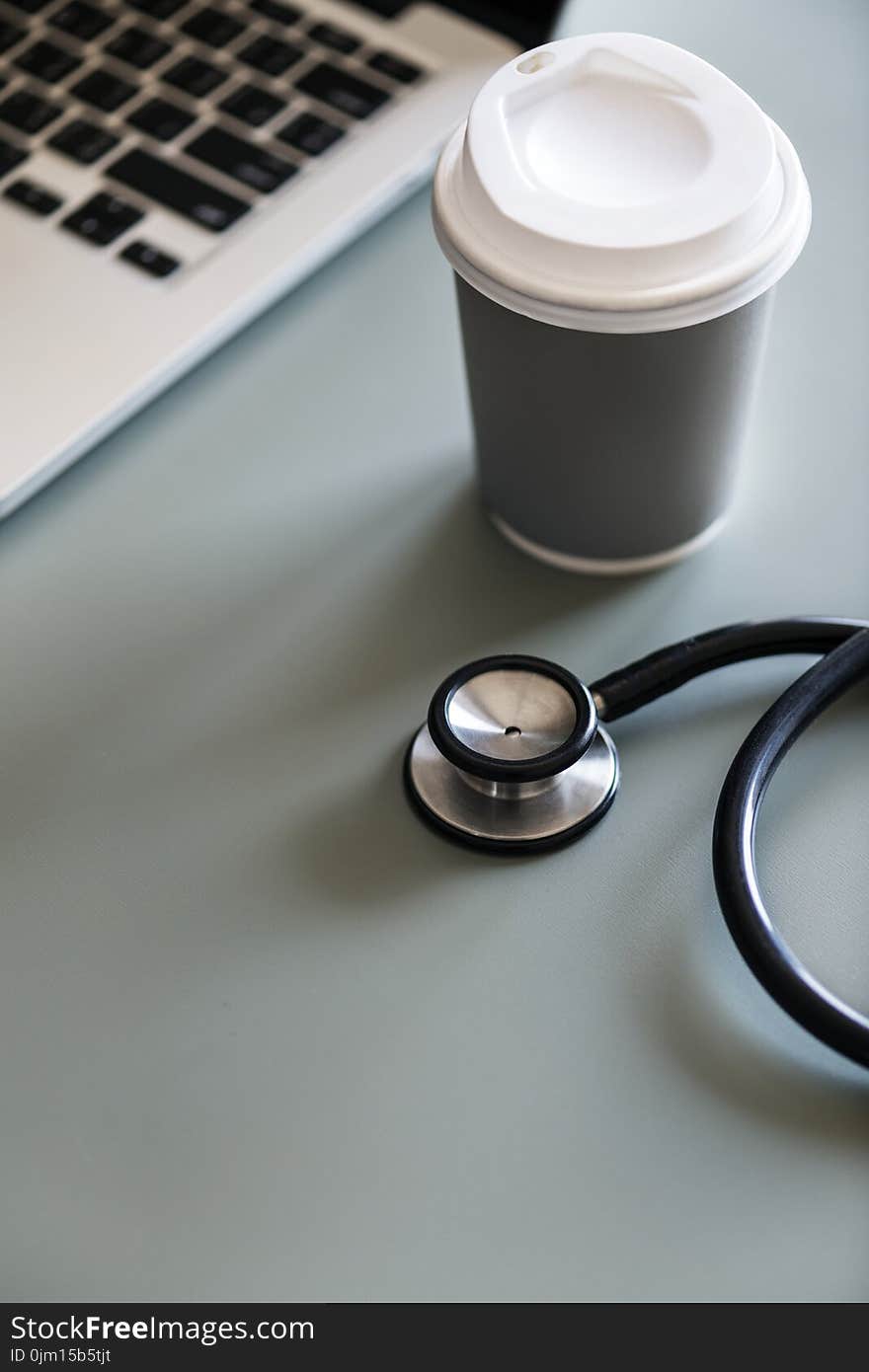 Black Stethoscope Beside Gray Disposable Cup