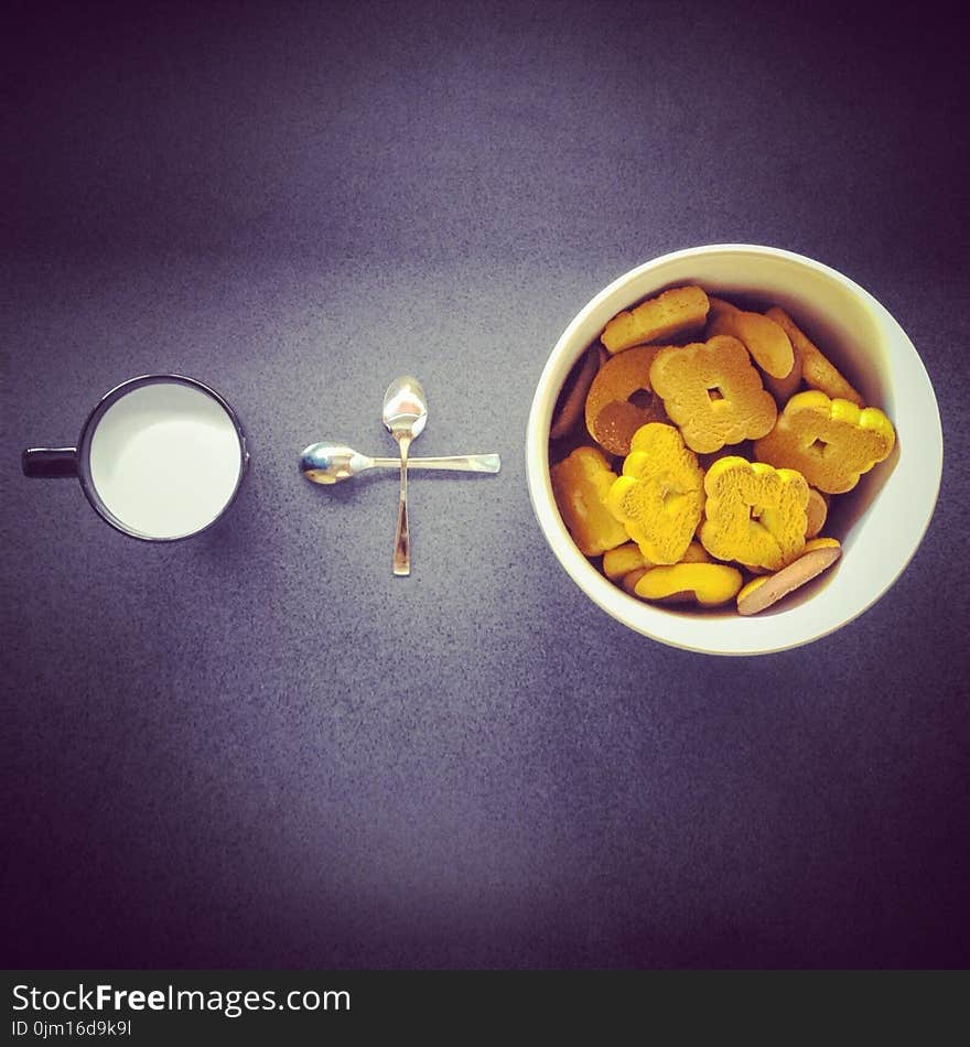 Crackers in Round White Ceramic Cup Near Two Stainless Steel Spoons and Black Ceramic Mug