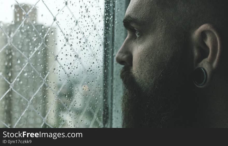 Selective Focus Photography of Man Staring on Glass Window Filled With Droplets