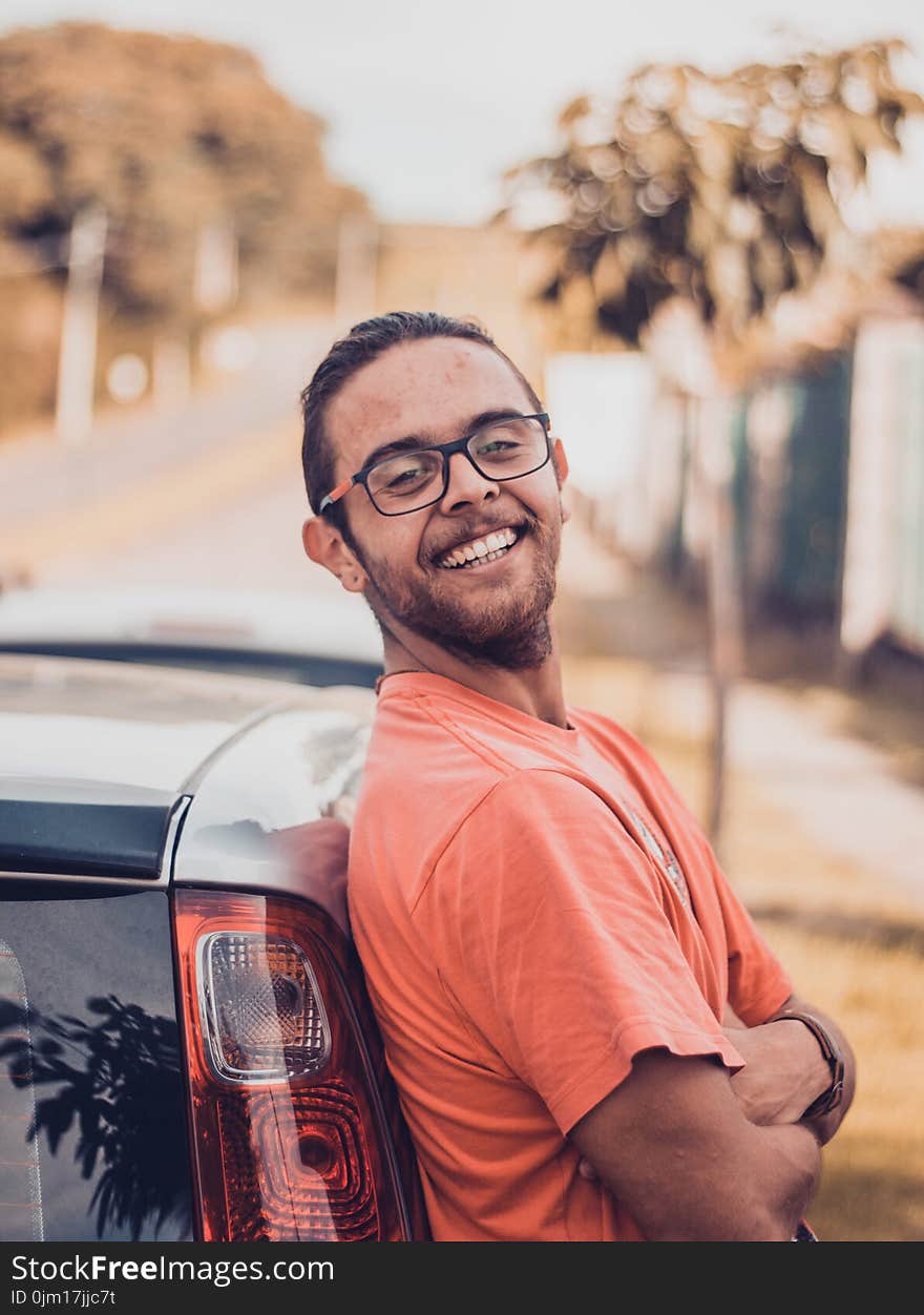 Man in Orange T-shirt Leaning on a Car