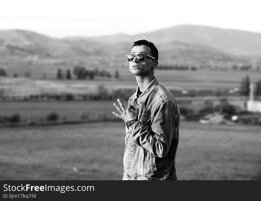 Grayscale Photo of Man Wearing Denim Jacket Near Mountain at Daytime