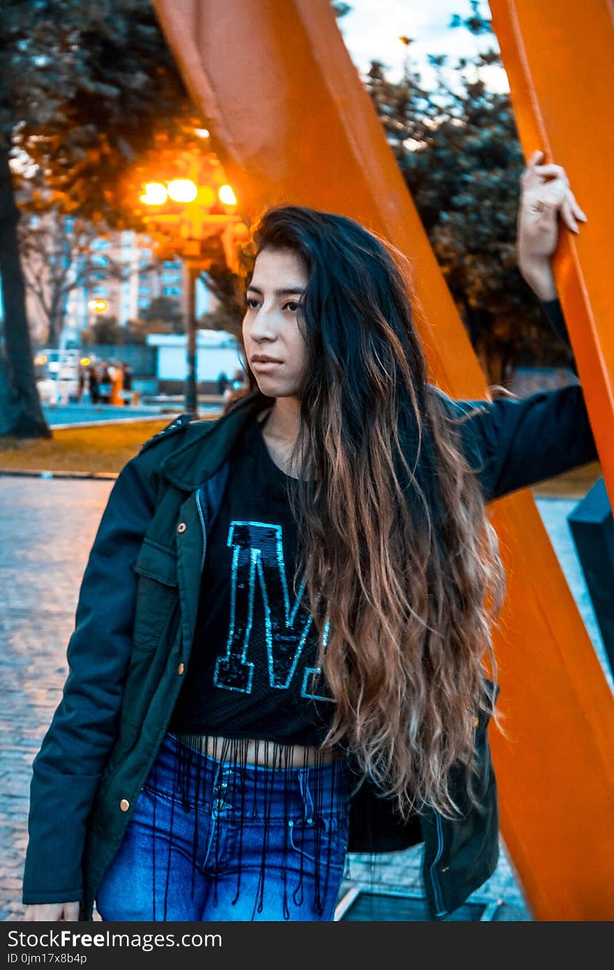 Woman Wearing Black Jacket Leaning on Orange Metal